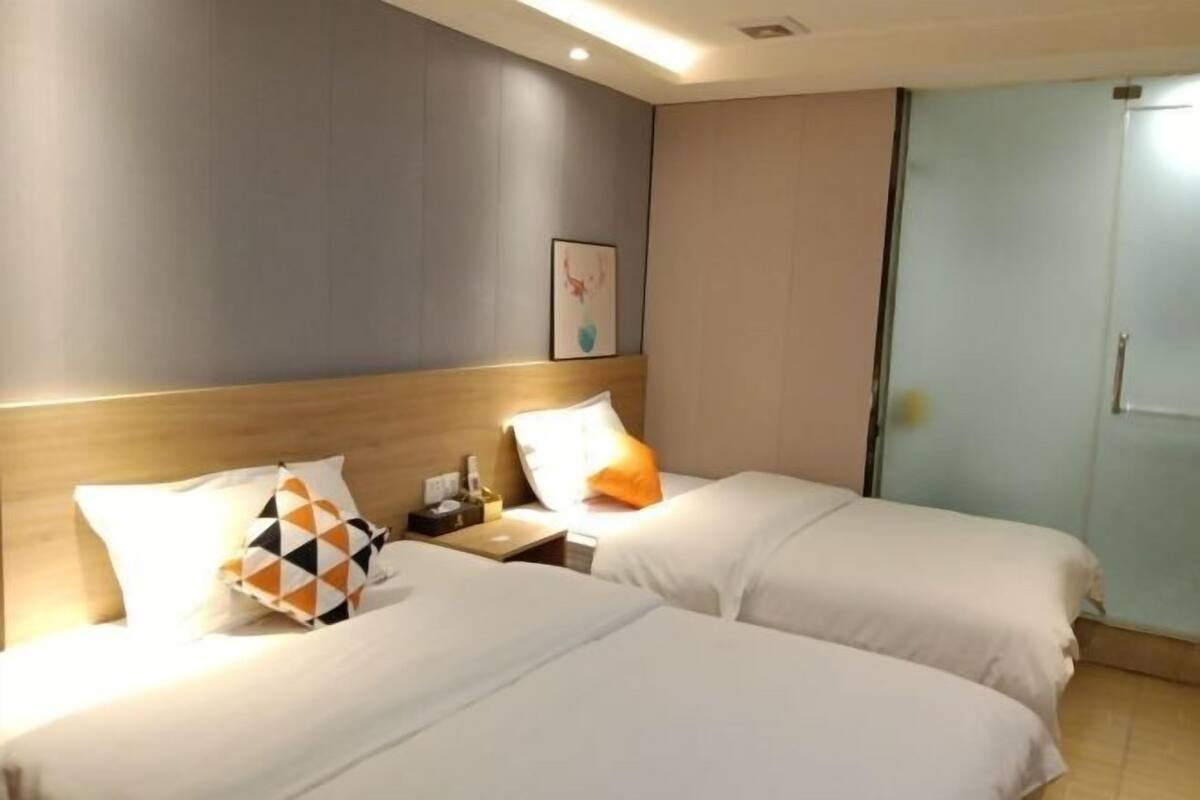 A hotel room with two beds, a nightstand, a lamp, and a framed picture on the wall.