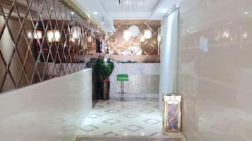 Un vestíbulo de hotel con una recepción, un letrero verde y una planta decorativa.