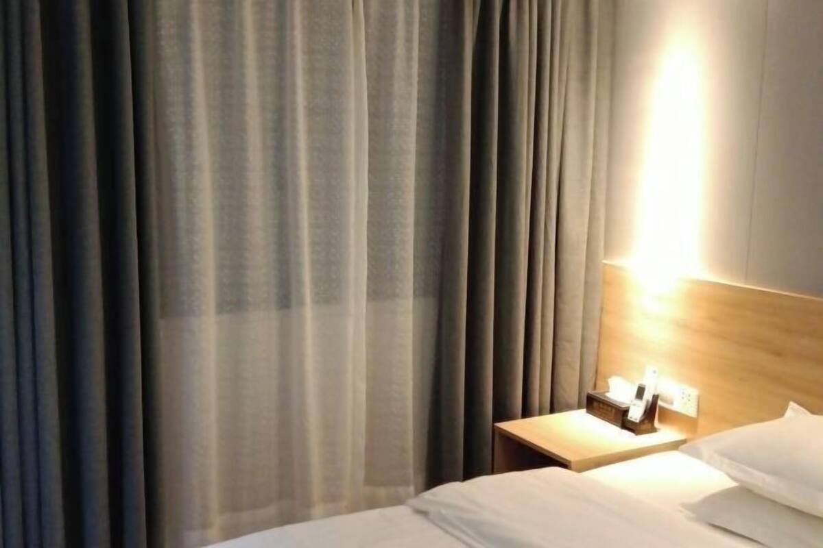 A hotel room with a bed, a nightstand with a phone and a lamp, and a curtain.