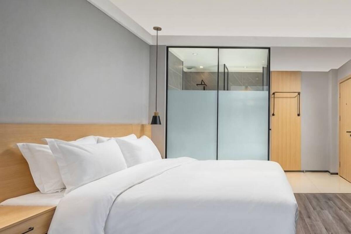 A modern hotel room with a large bed, a wardrobe, and a small desk.
