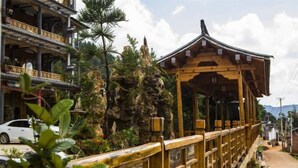 A traditional wooden structure with a curved roof, surrounded by lush greenery and a rocky backdrop. - Jizushan Funinglou Boutique Inn (Binchuan)