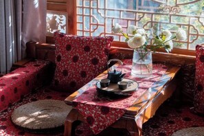 A traditional room with a wooden bench, a table with a red patterned tablecloth, and a vase with white flowers.