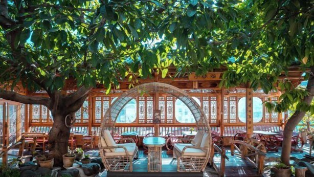 An outdoor seating area with wicker furniture and a wooden pergola, surrounded by potted plants and a traditional Asian architectural backdrop. - Jizushan Funinglou Boutique Inn (Binchuan)