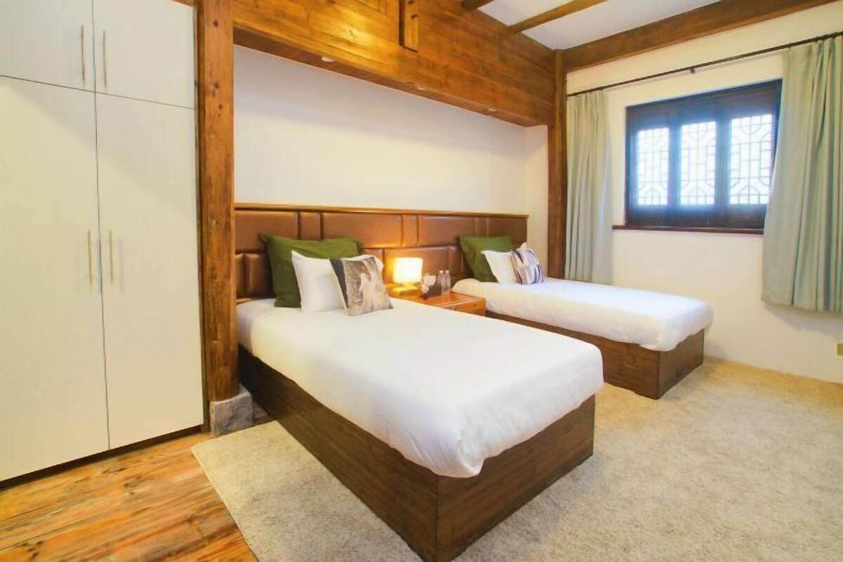 A bedroom with two single beds, a wooden headboard, a window with curtains, and a wardrobe.