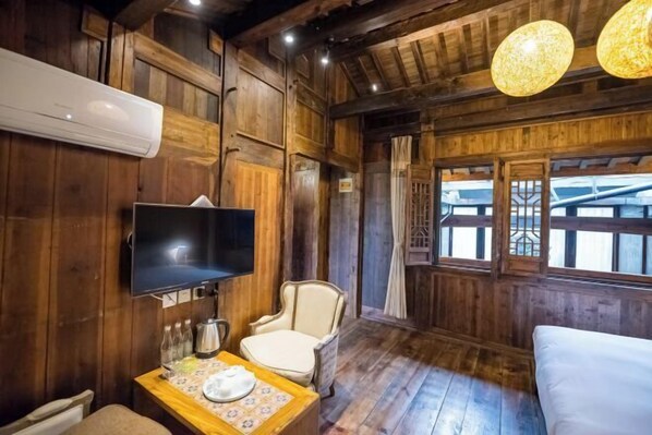 A wooden room with a television, a table with a plate, a chair, and a bed. - Hongcun Tachuan Alina Garden Vacation Apartment (Yi County)