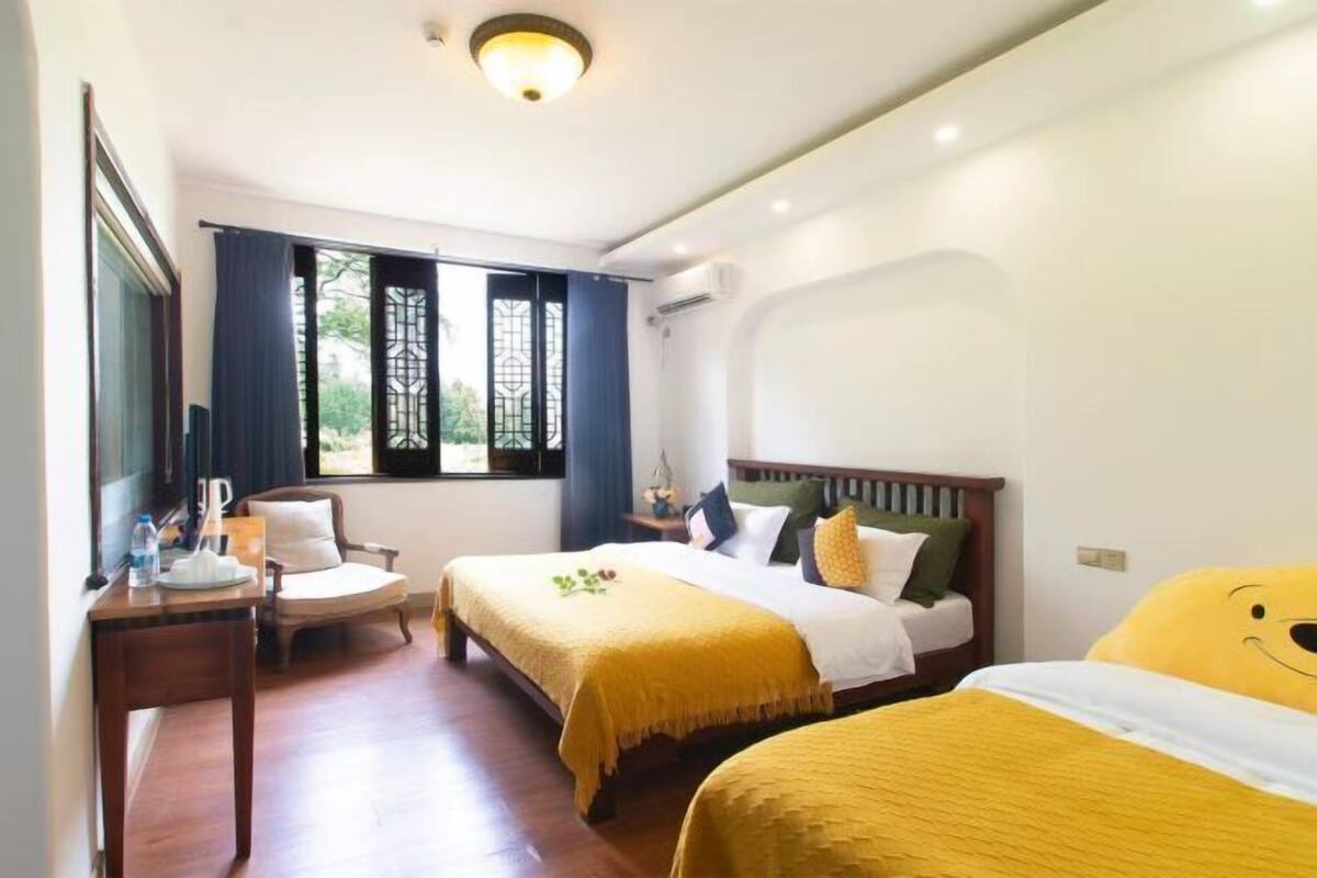A hotel room with two beds, a wooden desk, a chair, and a large window with curtains.