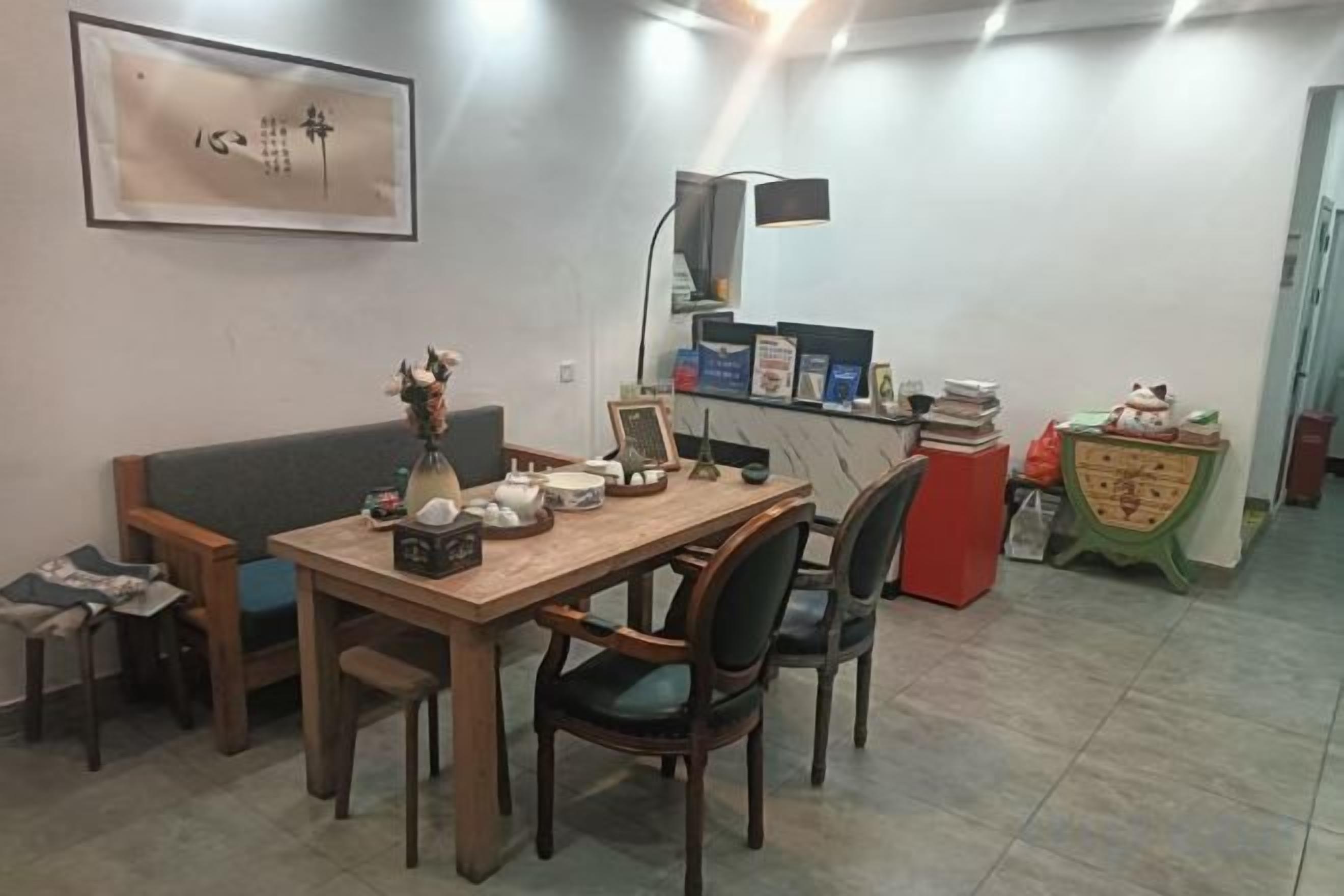 A dining area with a wooden table, chairs, and a sofa. There is a wall-mounted artwork and a small table with decorative items.