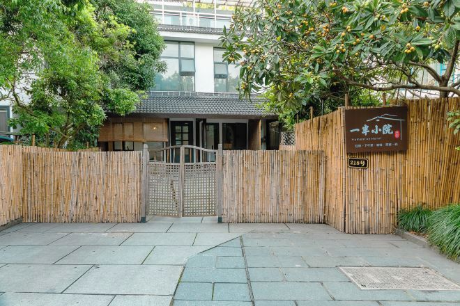 Una entrada tradicional al estilo japonés, con una puerta de bambú, un cartel y un sendero que conduce a un edificio con tejado de tejas.
