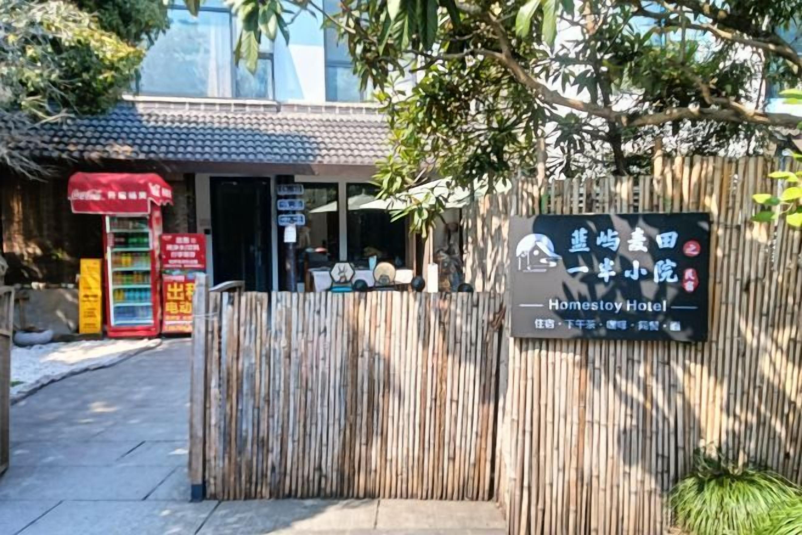 A hotel entrance with a bamboo fence, a signboard with hotel name, and a traditional building in the background.