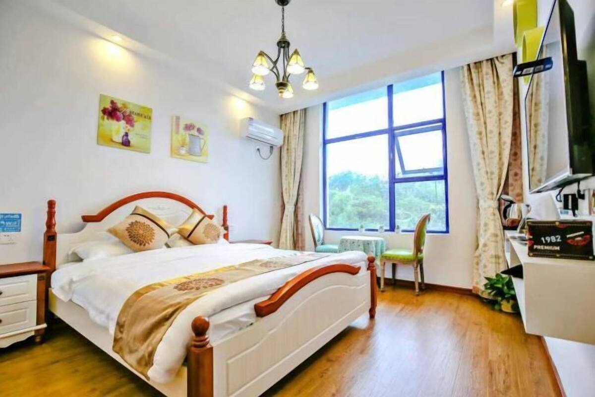 Ein Schlafzimmer mit einem hölzernen Bett, einem Schreibtisch, einem Stuhl, einem Fenster mit Vorhängen und einem Fernseher.