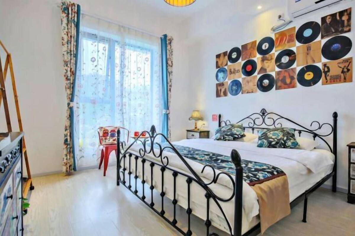 Ein Schlafzimmer mit einem Bett, einer Wand voller Schallplatten, einem Fenster mit Vorhängen und einem Schreibtisch mit Stuhl.