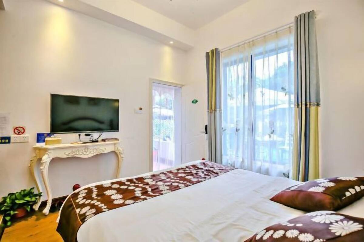 Ein Hotelzimmer mit Bett, Fernseher auf einem Schrank, einer Tür und einem Fenster mit Vorhängen.