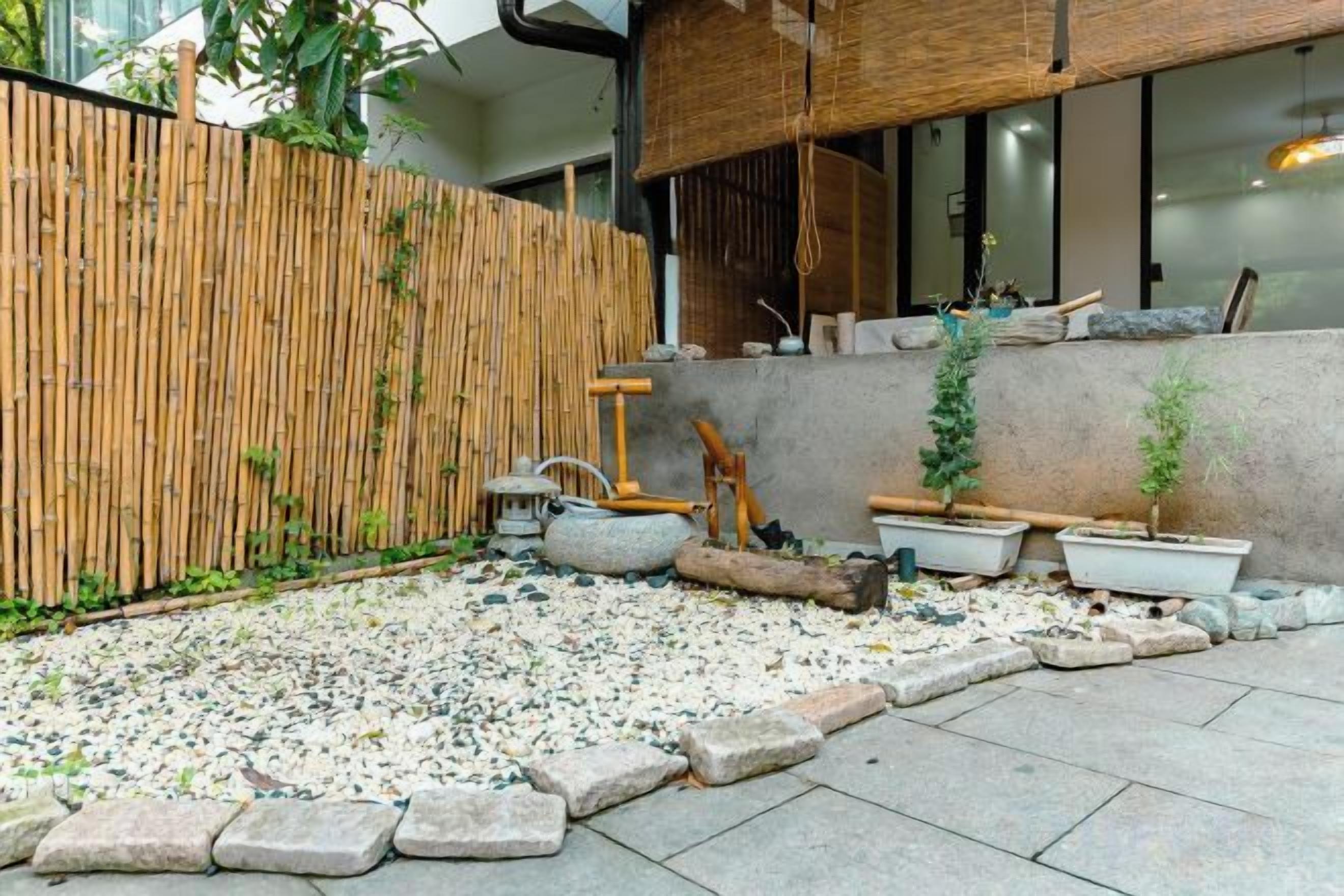 Un jardín con valla de bambú, plantas en macetas y un sendero de piedra.