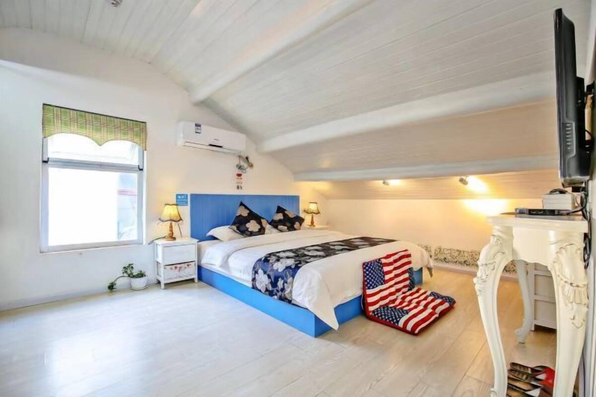 Ein Schlafzimmer mit Bett, Nachttischen, einem Fernseher und einem Fenster mit Vorhängen.