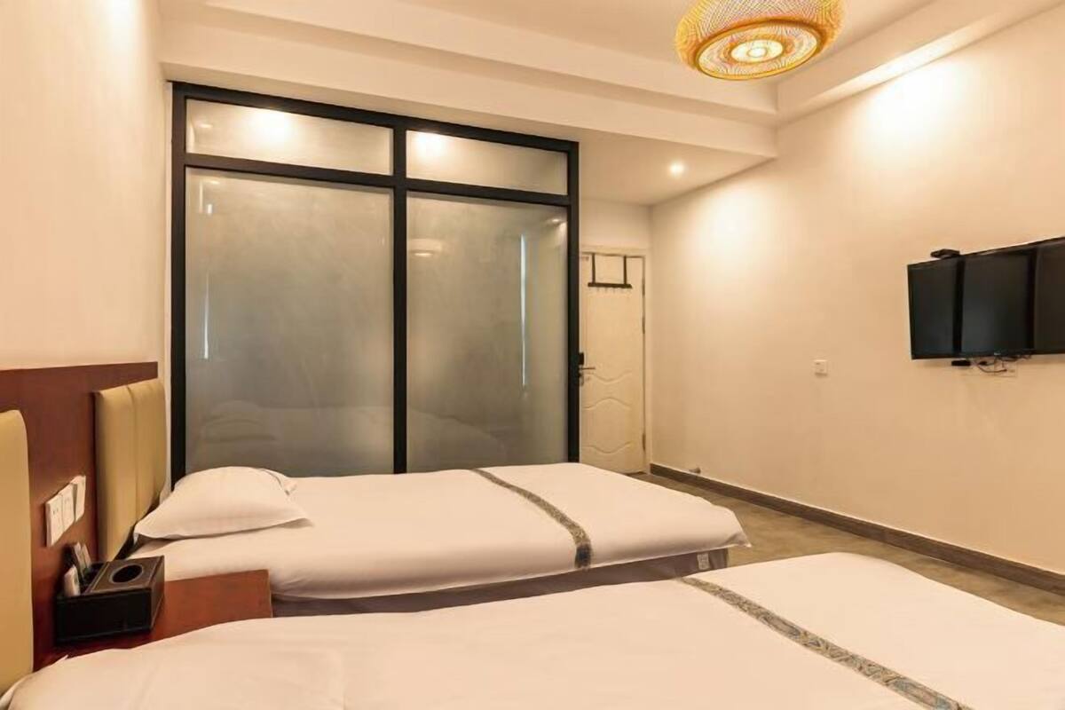 Ein Hotelzimmer mit zwei Betten, einer Schiebetür, einem Flachbildfernseher und einer Deckenleuchte.