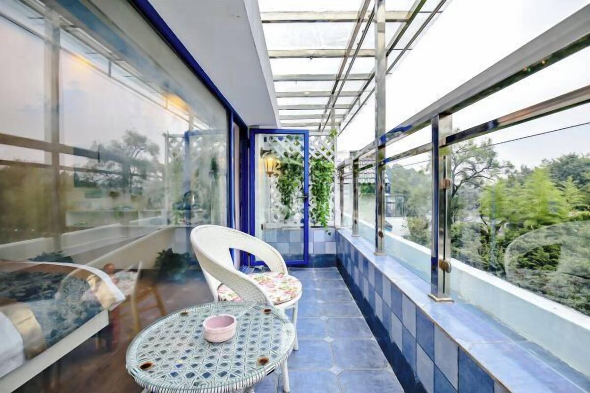 Ein Balkon mit Glasveranda, zwei Korbstühle, ein runder Tisch mit einer Schale und Blick auf Grünflächen.