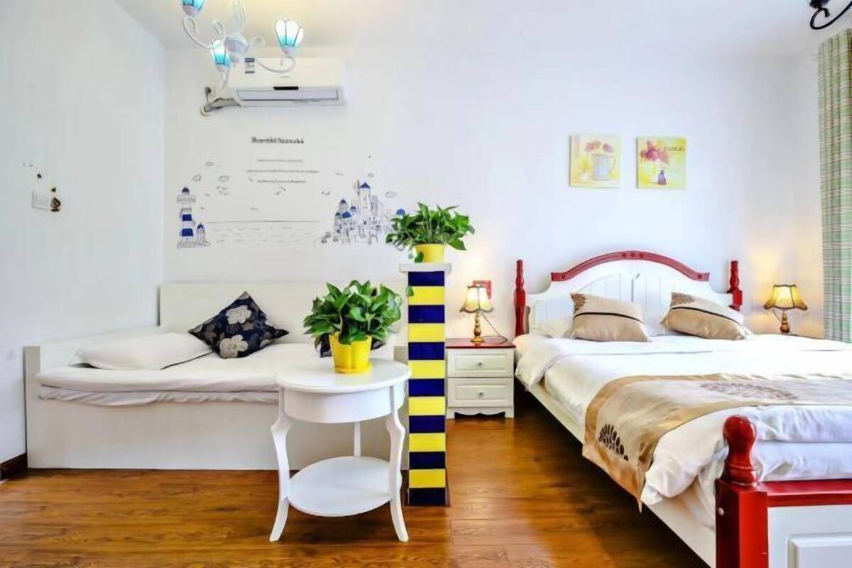 Ein Schlafzimmer mit Bett, Nachttischen, einer Wand-Klimaanlage, einem kleinen Tisch mit Pflanze sowie einer Wand mit Karte und Kunstwerken.