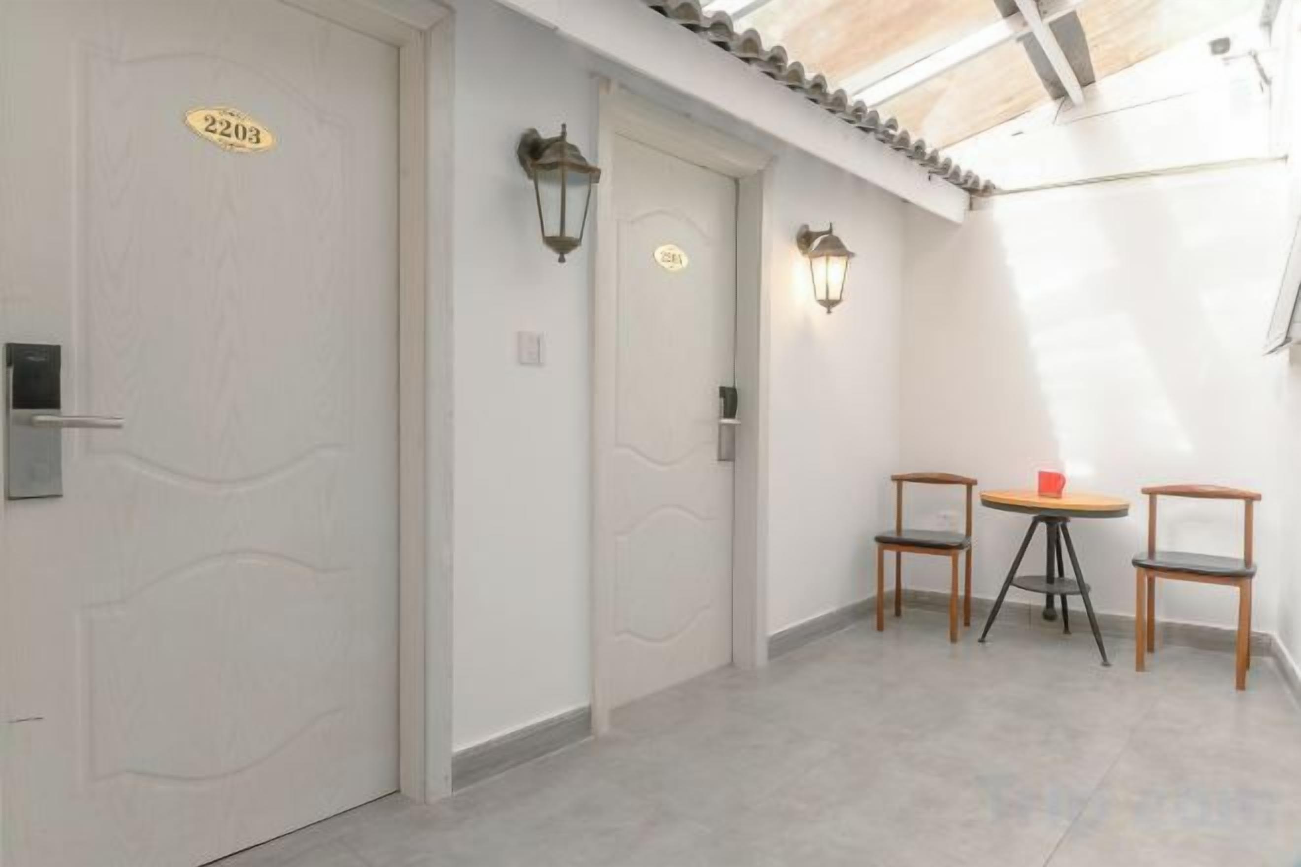 Un pasillo con dos puertas, cada una con un número. Hay dos sillas y una pequeña mesa con un objeto rojo encima.