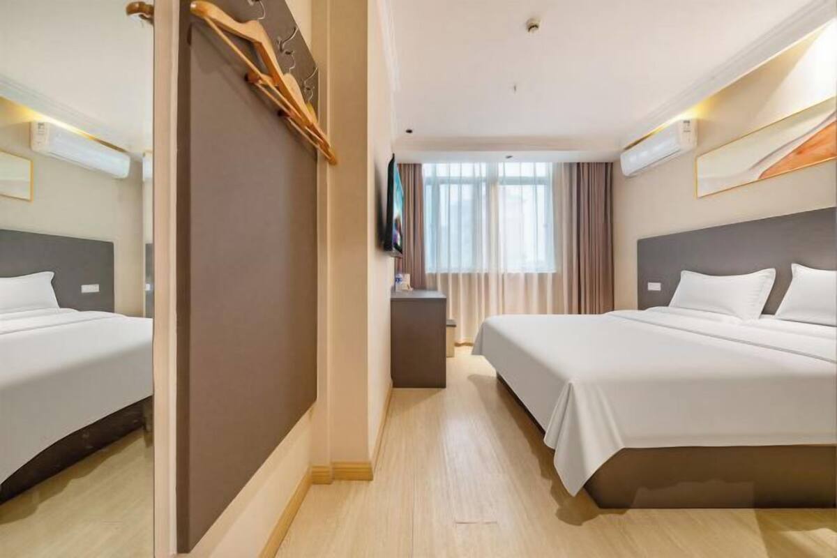 Ein Hotelzimmer mit zwei Betten, einem Schreibtisch, einem Fernseher und einem Fenster mit Vorhängen.