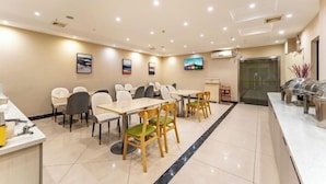 Zona ristorazione di un hotel con tavoli, sedie, un buffet e una televisione appesa al muro.