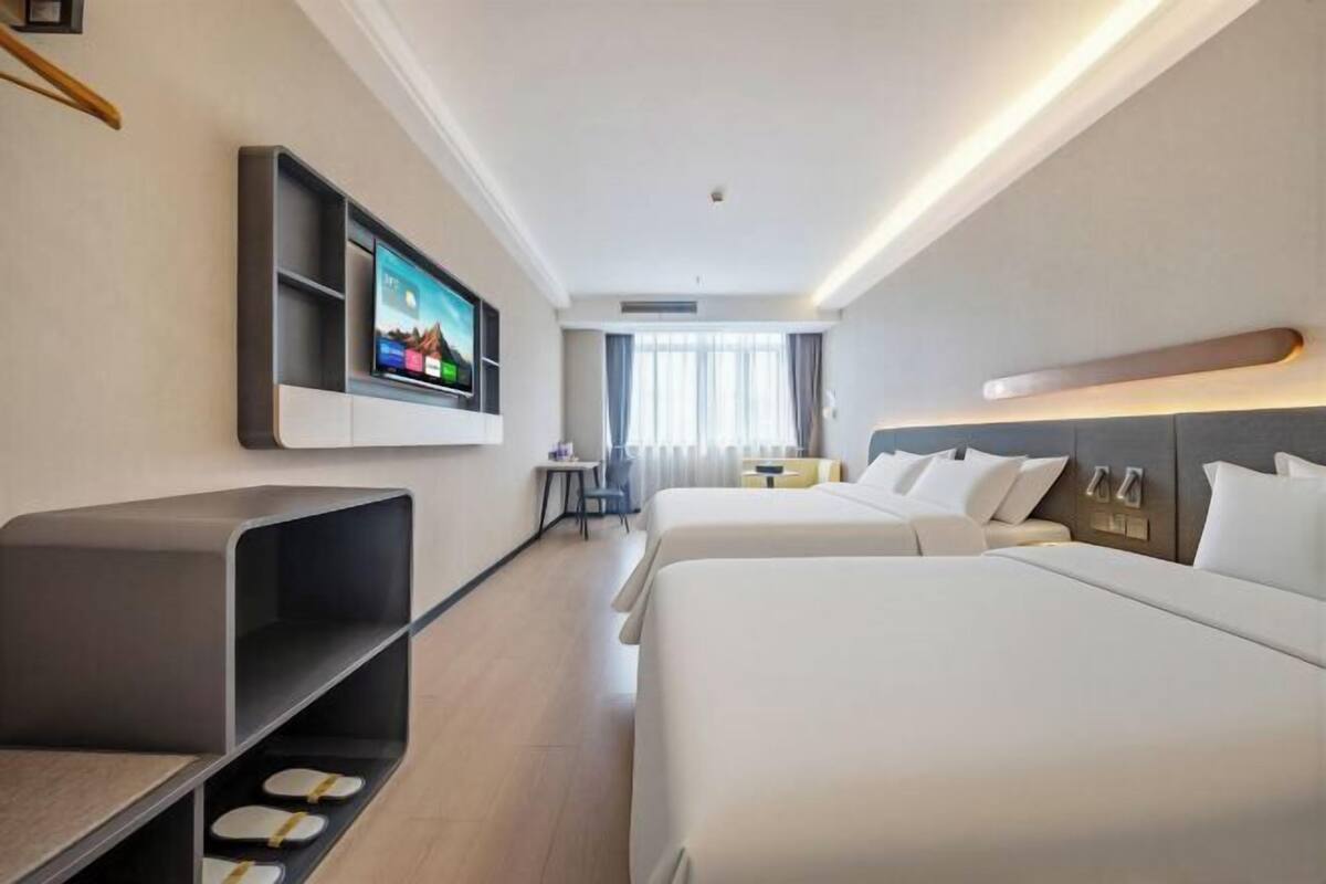 Ein Hotelzimmer mit zwei Betten, einem Wandfernseher, einem kleinen Tisch und einem Sessel.