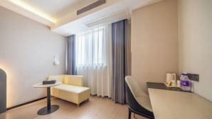 Camera d'albergo con divano, un piccolo tavolo rotondo, una sedia, un letto e una finestra con tende.