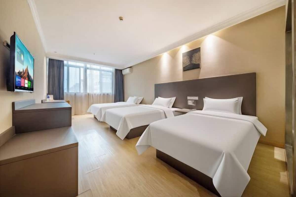 Ein Hotelzimmer mit zwei Betten, einem Schreibtisch, einem Flachbildfernseher und einem großen Fenster.