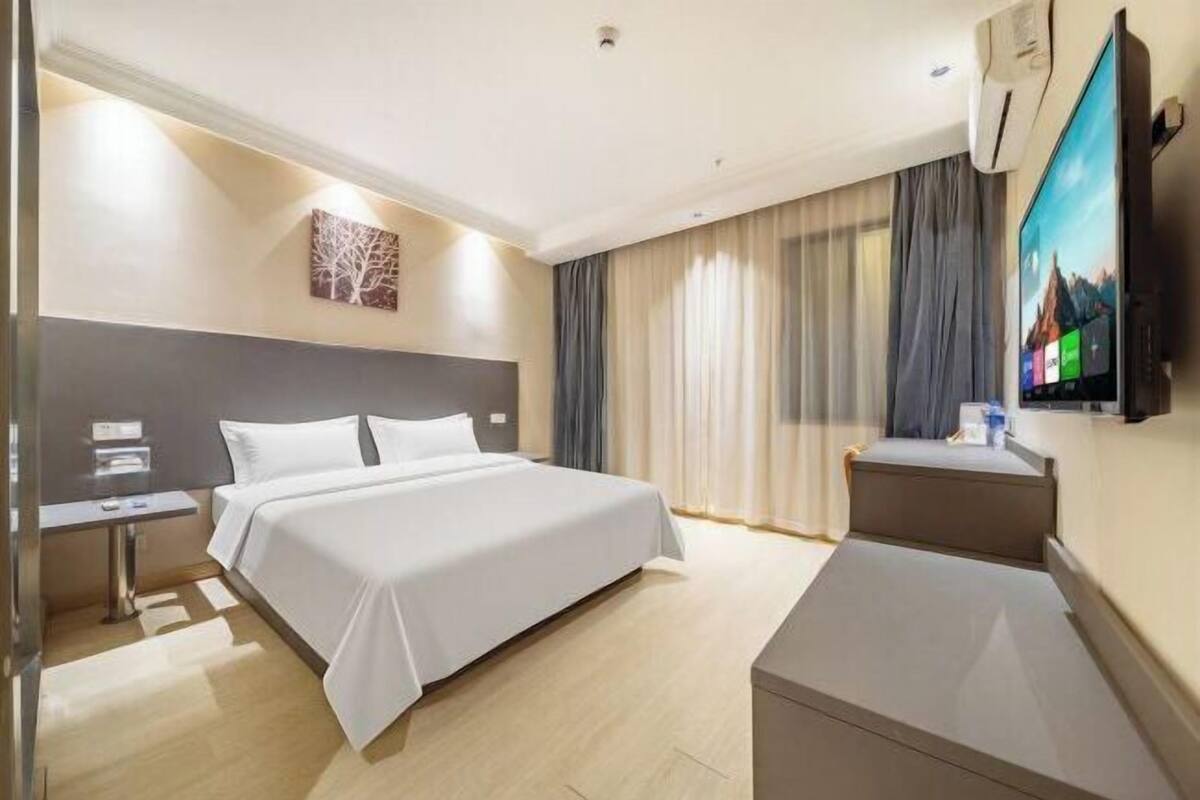 Ein Hotelzimmer mit Bett, Schreibtisch, Fernseher und einem Fenster mit Vorhängen.