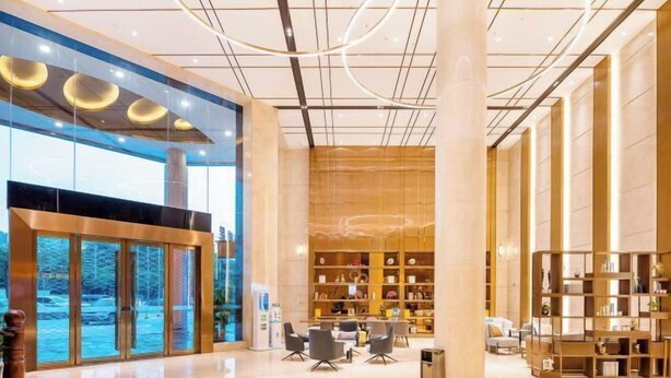 Un vestíbulo amplio con diseño moderno, que cuenta con una entrada de vidrio grande, una zona de estar central y una estantería bien organizada.
