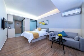A modern hotel room with a bed, sofa, and a small table with a vase.