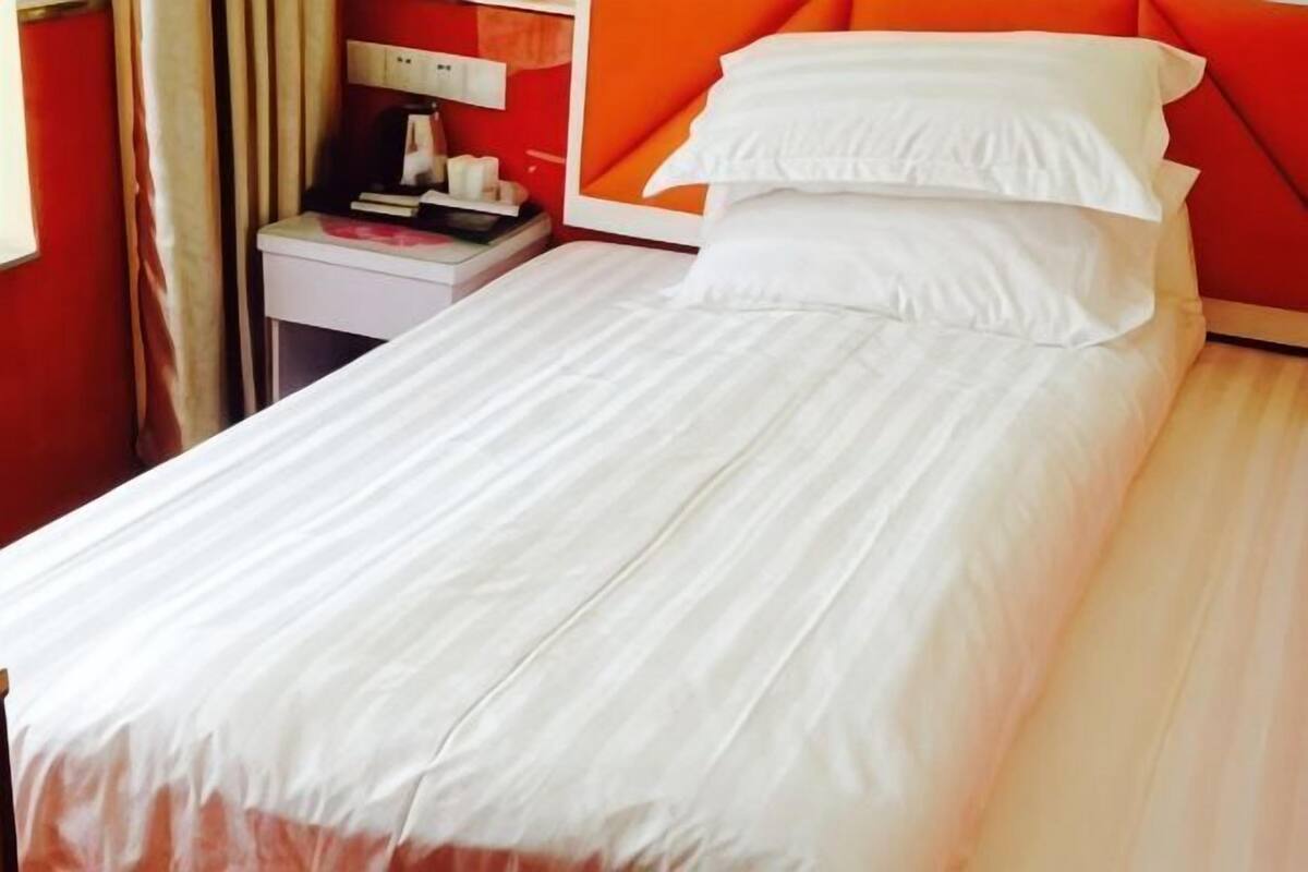 Ein Einzelbett mit weißer Bettwäsche in einem Zimmer mit roten Wänden und einem Holz-Kopfteil.