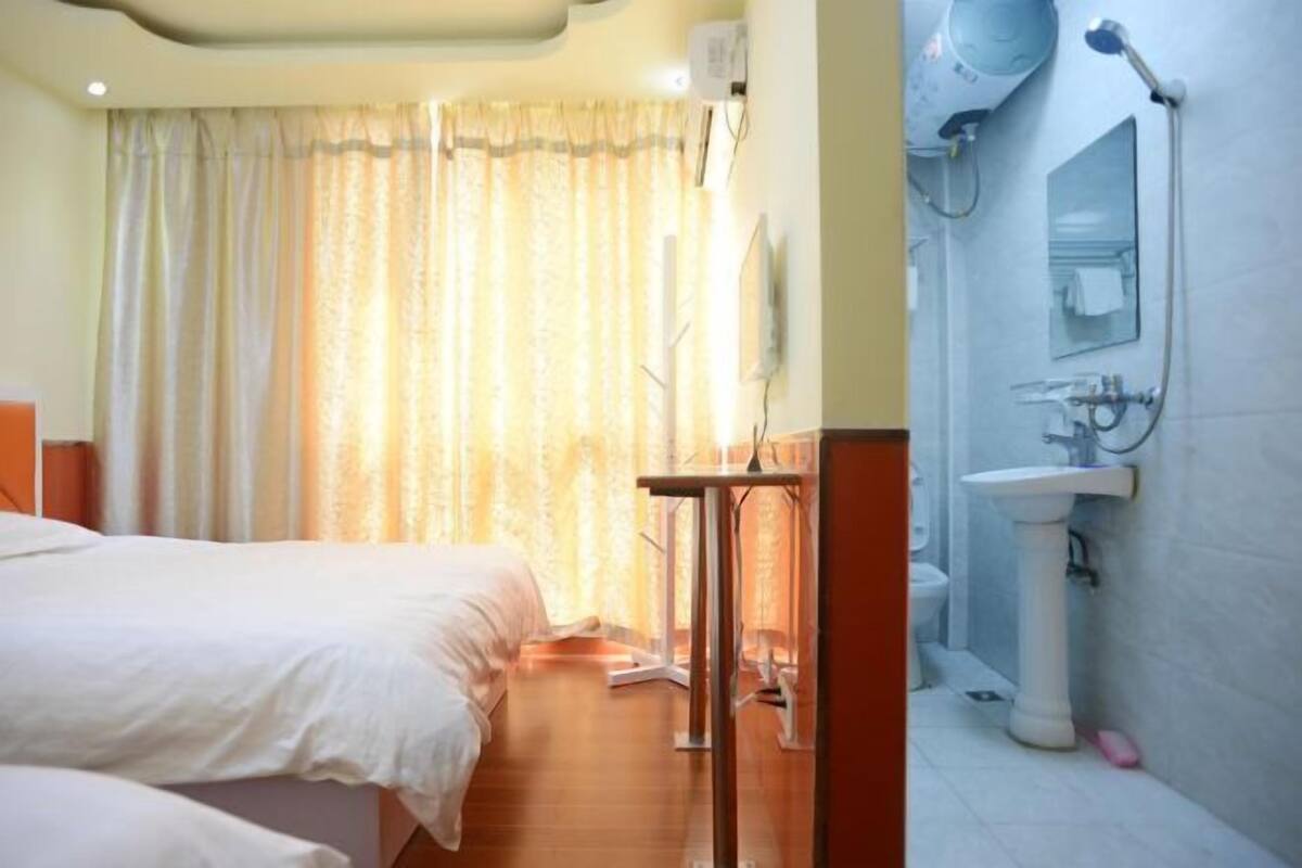 Ein Hotelzimmer mit Bett, Schreibtisch, Stuhl, einem Fenster mit Vorhängen, einem Waschbecken und einem Spiegel.