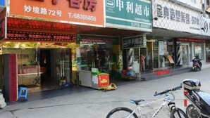 Vista de la calle con un hotel llamado "Hotel Qianqian" a la izquierda, una tienda de conveniencia "Shijie Supermarket" en el centro y un spa llamado "Gold Classic Spa" a la derecha.