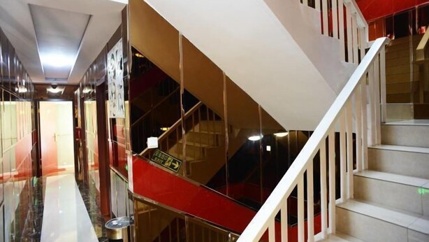 Un interior moderno con una escalera, barandas de vidrio y una pared de acento roja.
