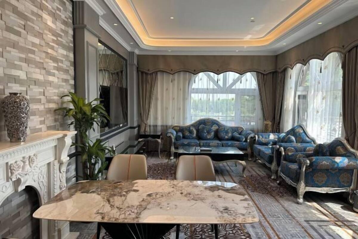 A luxurious living room with a marble coffee table, blue upholstered sofas, and a fireplace.
