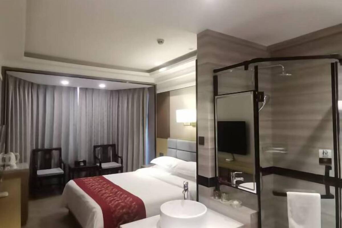 A hotel room with a bed, a desk, a chair, a shower, and a bathroom.