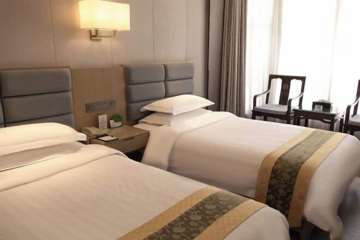 A hotel room with two beds, a nightstand, a lamp, a chair, and a table.