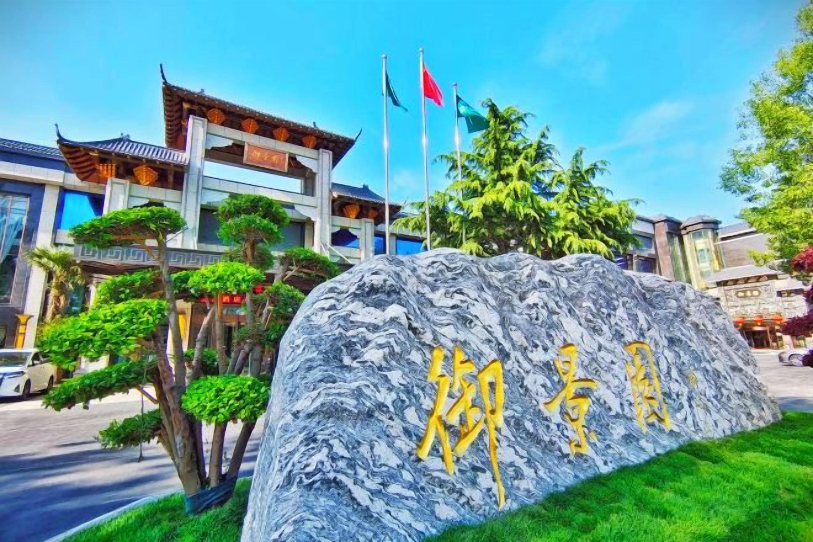 A stone sign with Chinese characters, a traditional building with a tiled roof, and flags.