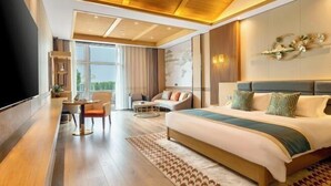 Ein modernes Hotelzimmer mit einem großen Bett, einer Sitzecke mit Sofa und Sesseln, einem Esstisch und einem großen Fenster mit Blick.