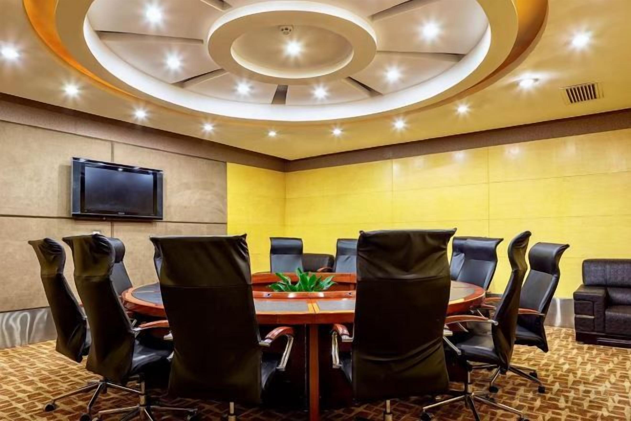 A conference room with a round table, black chairs, a flat-screen TV, and a yellow accent wall.