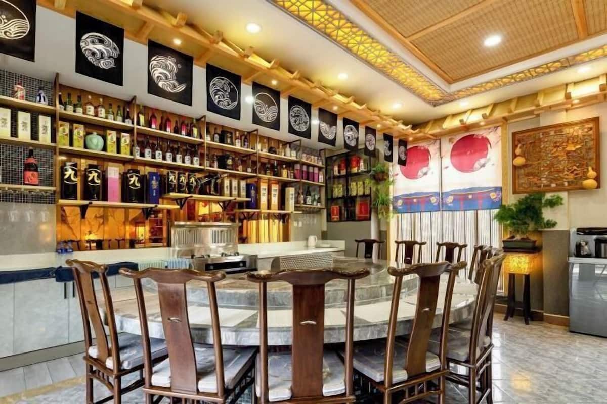 A restaurant interior with a round table, wooden chairs, and shelves of bottles.
