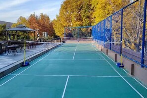 An outdoor tennis court with a net, surrounded by a blue fence and trees with autumn foliage. - Yujing Garden Holiday Hotel (Shijiazhuang)