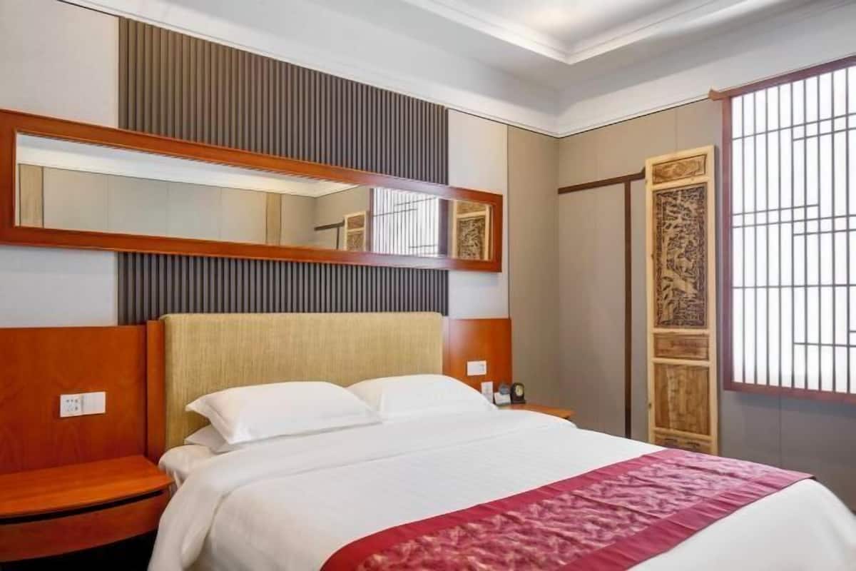 A hotel room with a bed, wooden headboard, bedside tables, a mirror, and a decorative panel.