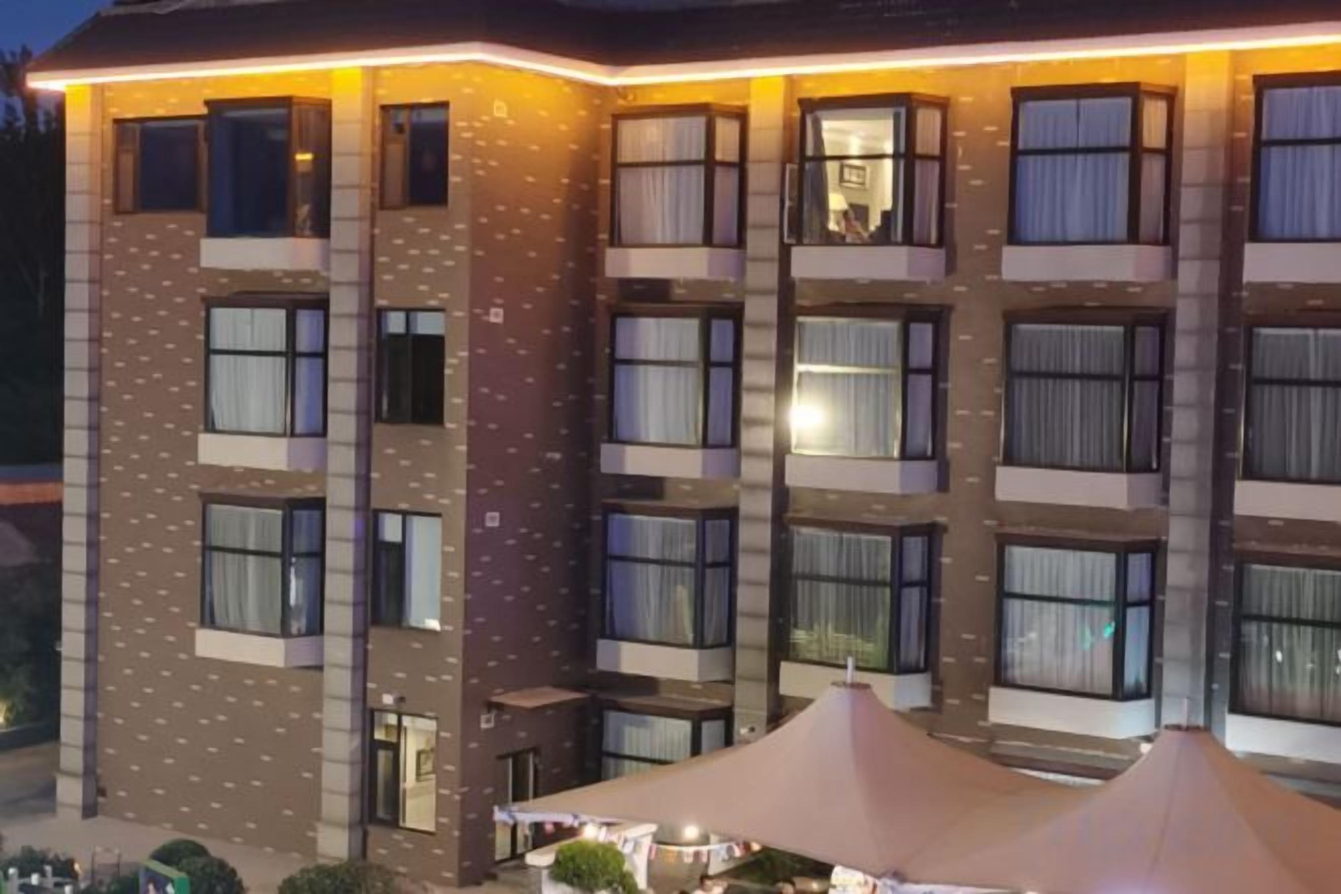 Um hotel com vários andares, fachada moderna, janelas amplas e área externa coberta com mesas e cadeiras.
