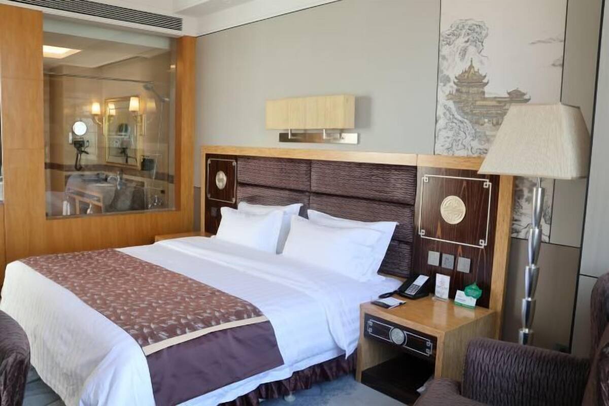 A hotel room with a large bed, a bedside table with a lamp, a mirror, and a wall-mounted light fixture.
