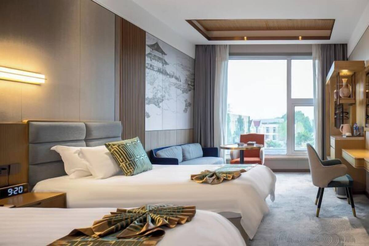 A hotel room with a large bed, a desk, a chair, and a view of the city.