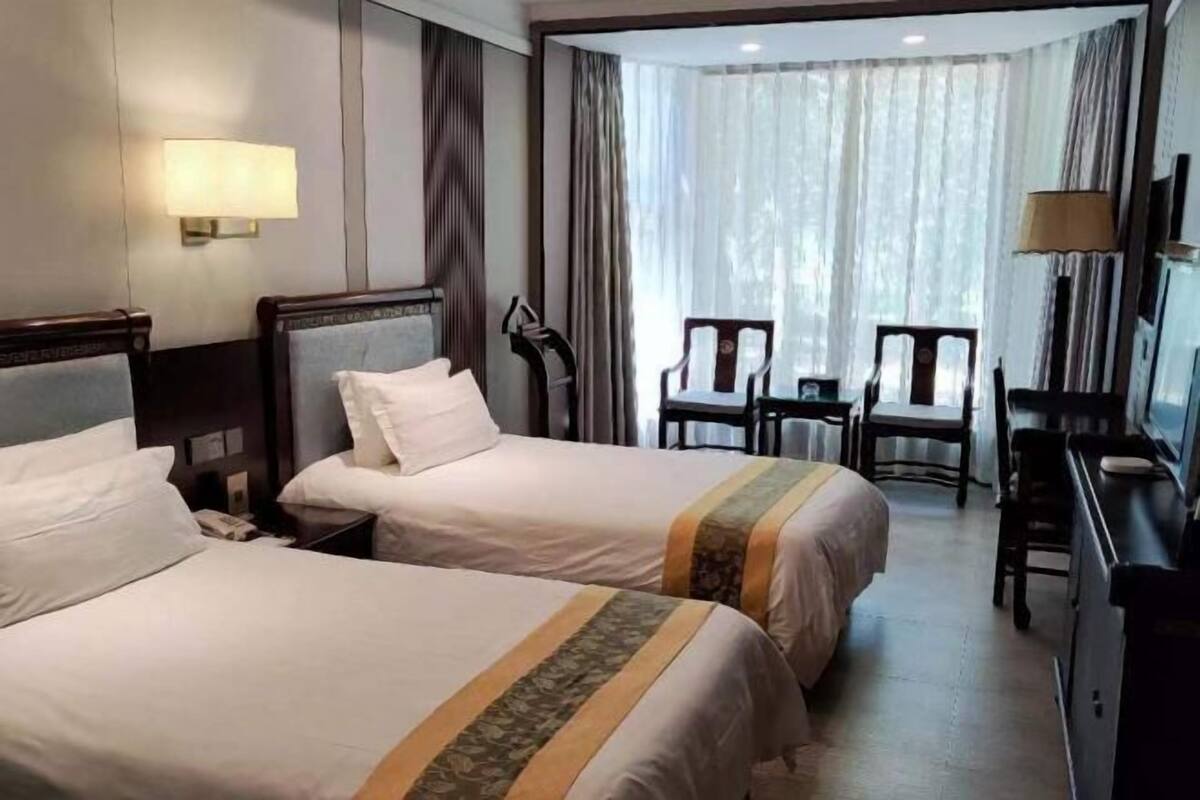 A hotel room with two beds, a desk, a chair, and a TV.
