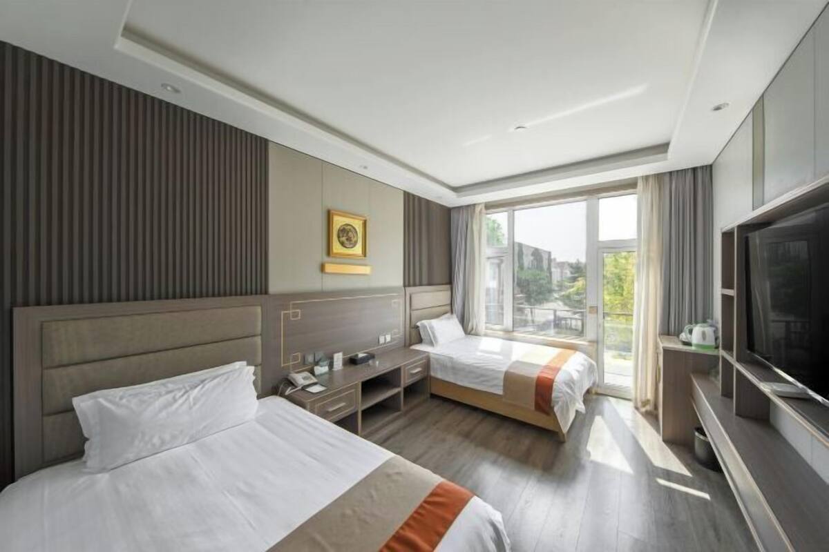 A hotel room with two beds, a desk, a TV, and a large window.
