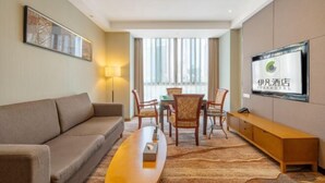Ein Hotelzimmer mit einer Couch, einem Esstisch mit Stühlen, einem an der Wand befestigten Fernseher und einem großen Fenster.