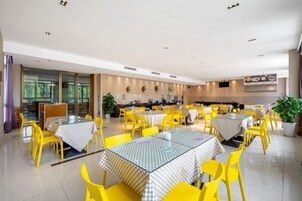 Un comedor amplio con varias mesas y sillas, una cocina al fondo y ventanas grandes que dejan entrar luz natural.